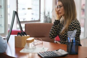 Woman in glasses staring at her face in table mirror