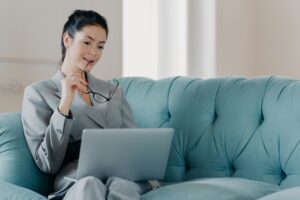 Serious woman entrepreneur takes off glasses, focused in laptop computer screen