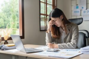 Upset woman touching head using calculator and laptop for calculating finance. Frustration young