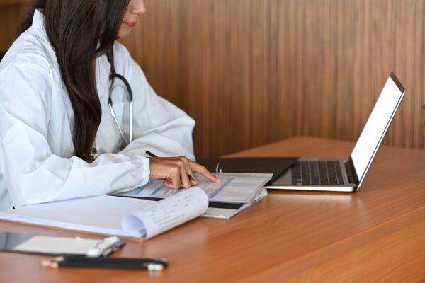 Female doctor working with computer laptop and reading medical informations on clipboard.
