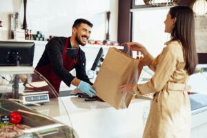 Shop assistant handling shopping bag to female customer in grocery store