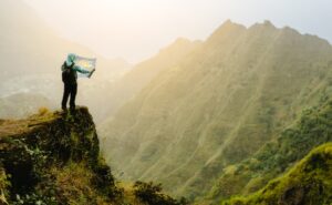 Man with the map staying on top of the mountain rock with gorgeous panorama view over high mountain